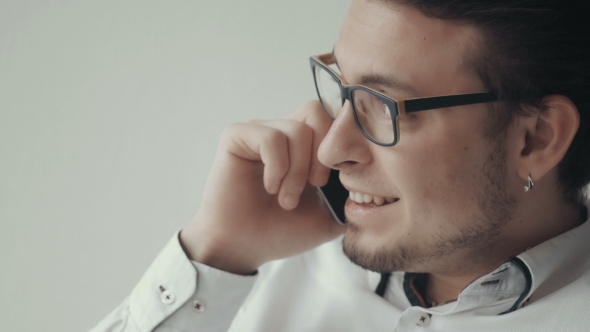 Portrait of Young Man in Glasses Talking on the Phone Against White Background