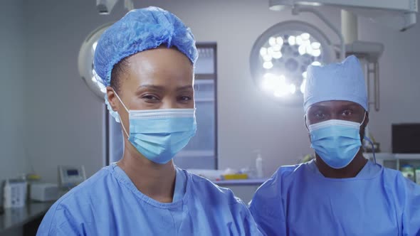 Portrait of diverse male and female surgeon wearing face masks standing in operating theatre