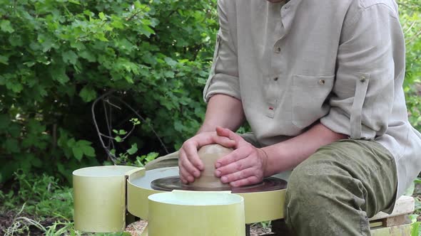 Caucasian Male Potter Sits at a Bench and Centers a Piece of Clay on a Rotating Circle and Moves It