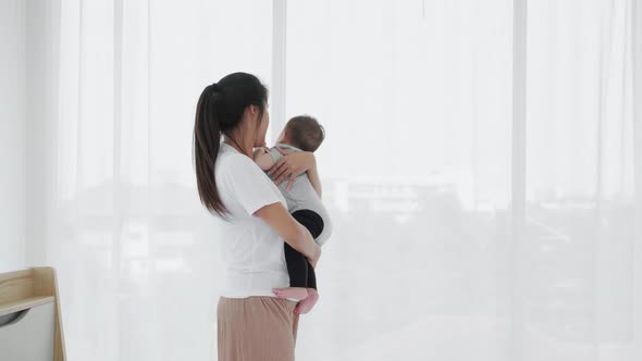 Happy Asian mother holding cute baby girl daughter playing in bedroom. Single mom concept