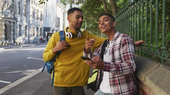 Two happy mixed race male friends standing and using smartphone in the street