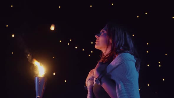 Woman watches as sky lanterns fly Into the night sky