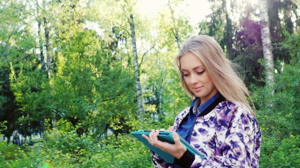 Young And Attractive Woman Walking With a Tablet On City Park