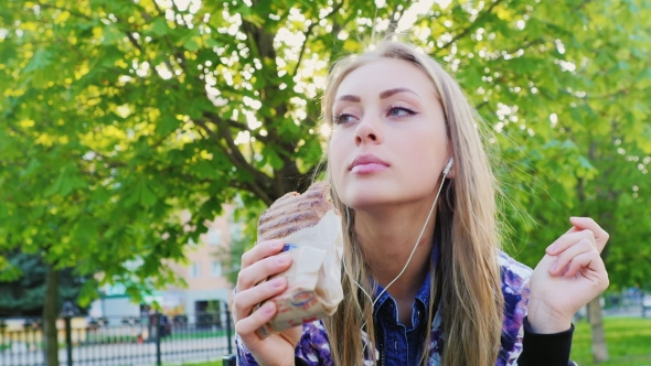 Attractive Woman Eating a Sandwich In The Park, Listening To Music