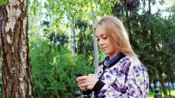 Attractive Young Woman Walking On City Park, Typing Sms On Smartphone
