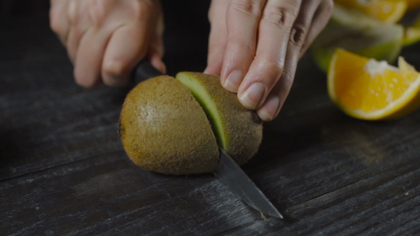 Chef Cuts Kiwi With Knife On Dark Wooden Table