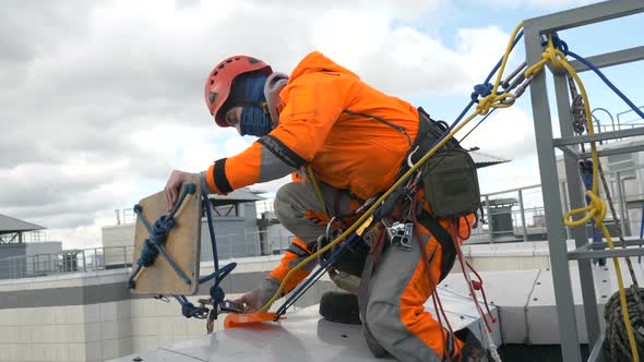 Industrial Climber in Suit Checks and Installs Seat and Insurance on Roof of Building Before Descent