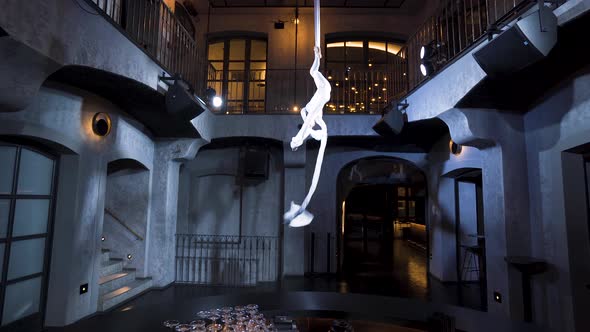 Female aerialist getting into a vertical split on silks above a bar.