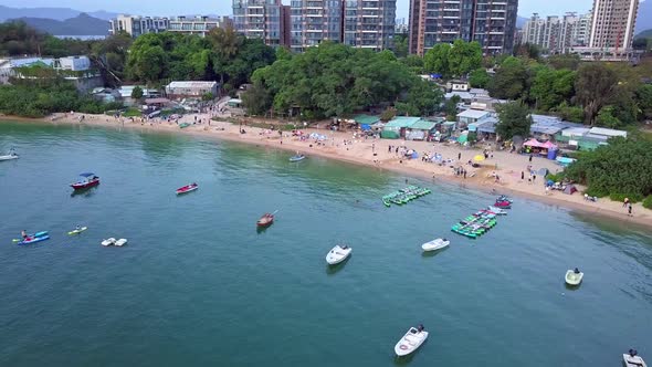 A dynamic tracking aerial shot of the Ma On Shan town beach with various buildings and boats near th