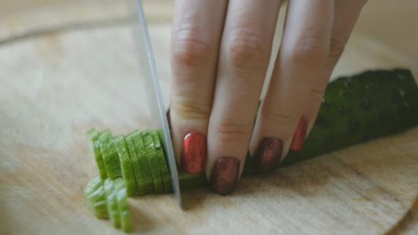 Girl's Hands With Red Nails Cut Cucumber Into Slices