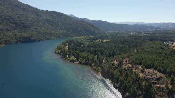 Aerial lowering on Epuyen lake between mountains covered in pine tree forest, Patagonia Argentina