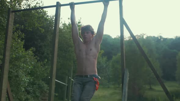 Young fit topless man doing knee raise exercise to strengthen core outdoor gym SLOW MOTION