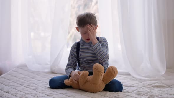 Wide Shot Autistic Boy with Teddy Bear Sitting on Bed at Home Showing Tongue Out Playing