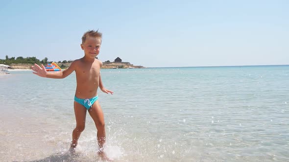 Little Boy Likes To Run Along the Seashore on a Sunny Day Creating Splashes in Different Directions