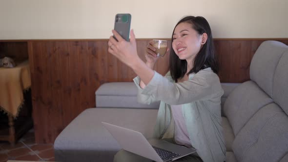 Smiling Asian woman taking selfie with latte on smartphone