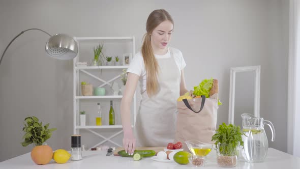 Confident Young Caucasian Woman Taking Out Fruits and Vegetables From Bag at Home