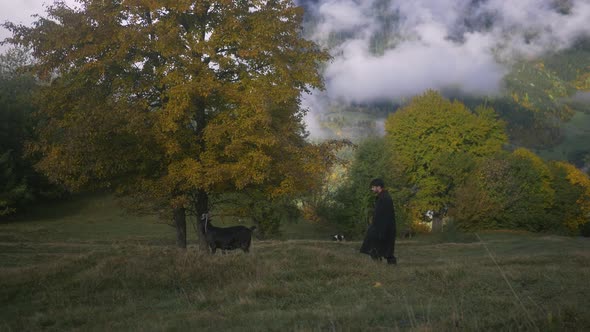 A Young Stylish Guy Walks with a Goat Near His House