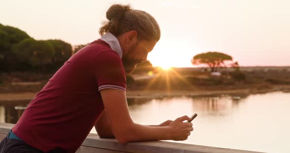 Caucasian Guy in Red Tshirt Texting with Sunset Skies in the Background