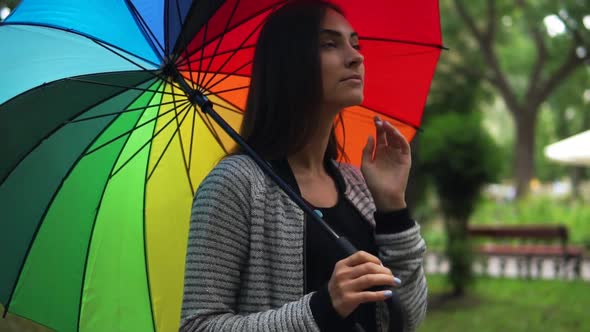 Portrait of a Young Beautiful Woman Walking with Colorful Umbrella in a Rainy Day in the City Park