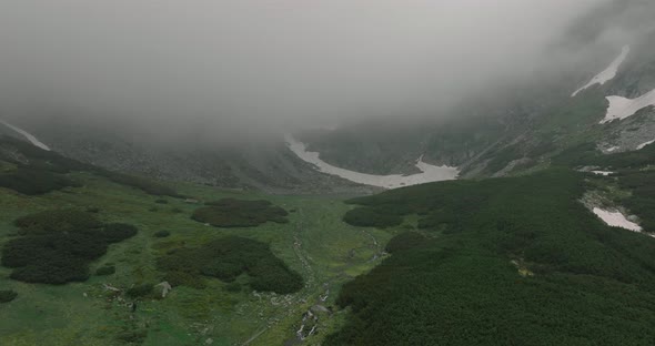 flying towards a mountain lake through clouds at the top of mountain with snow