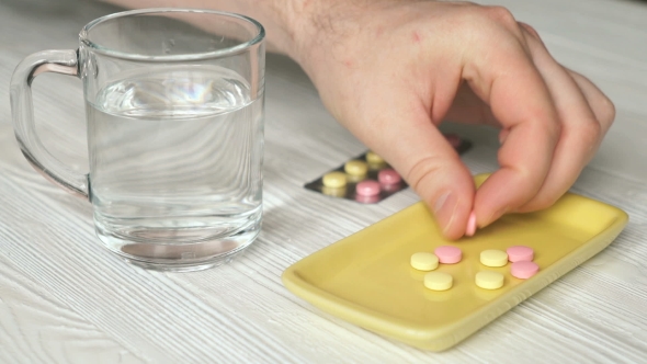 Man's Hand Takes The Pills From a Yellow Container