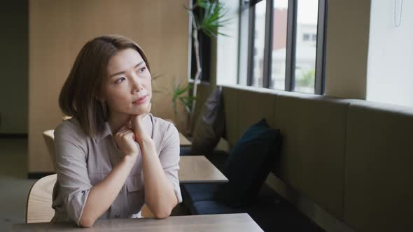 Asian businesswoman sitting looking out of window in modern office