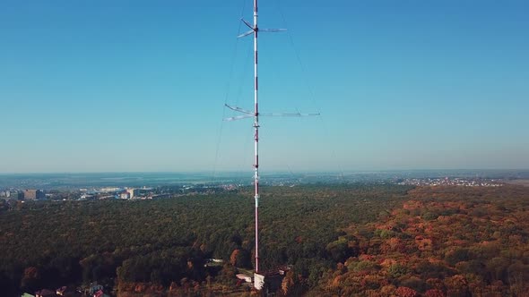 high telecommunication antenna on the background of forest and cityscape.