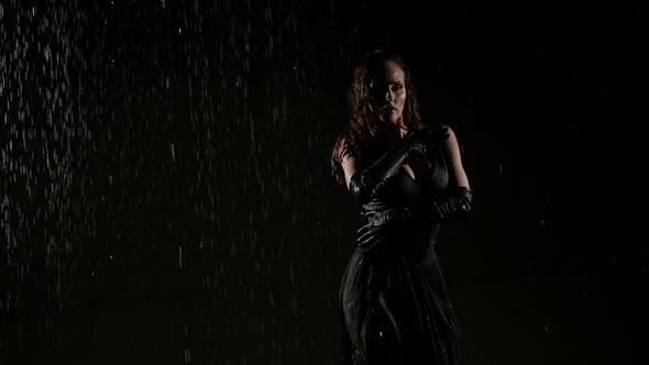 A Young Woman in a Sexy Black Suit Poses in a Dark Studio and in the Rain