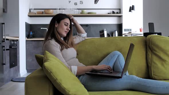 Relaxed Serious Woman Student Using Laptop Device Leaning on Sofa at Home Office, Focused