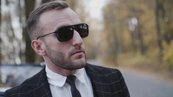 Portrait of Serious Man in Sunglasses and Suit Stands at Retro Car