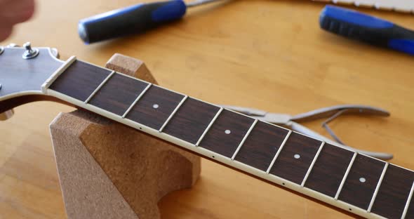 Close up hands of a luthier craftsman measuring and leveling an acoustic guitar neck fretboard on a