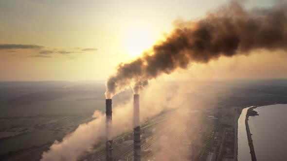 Aerial view of coal power plant high pipes with black smoke moving up polluting atmosphere at sunset alt