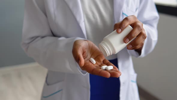 African American Female Doctor in White Coat Takes Pills Out of a Jar