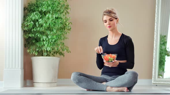 Smiling Fitness Woman Sitting in Lotus Position Eating Fresh Vegetable Salad Using Fork