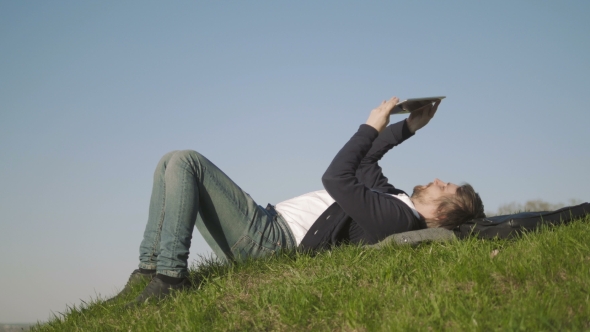 Side View Of Young Man Using Tablet PC While Lying On Grass Against Clear Sky