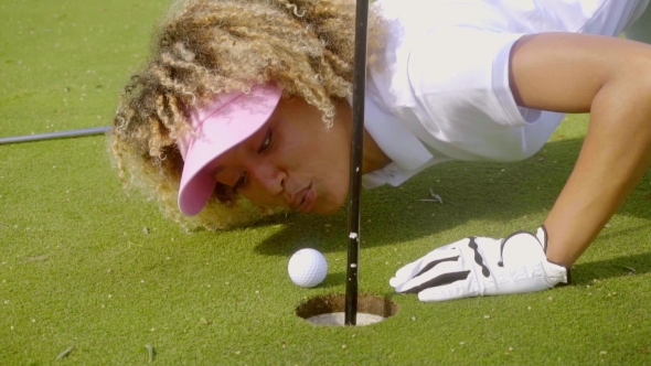 Young Woman Blowing Her Golf Ball Into The Hole