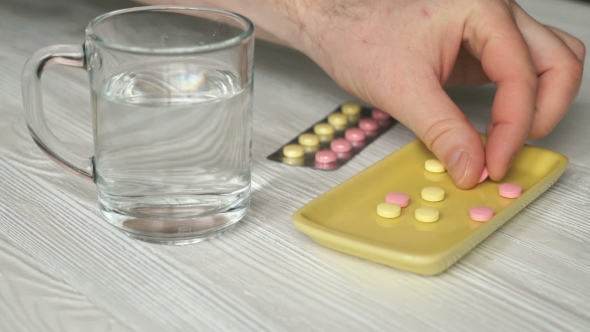Man's Hand Takes The Pills From a Yellow Container