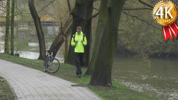 Man Scrolls a Tablet Near Bicycle in Park Tourist