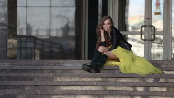 Girl Sitting On The Steps Of The City And Posing At The Camera 