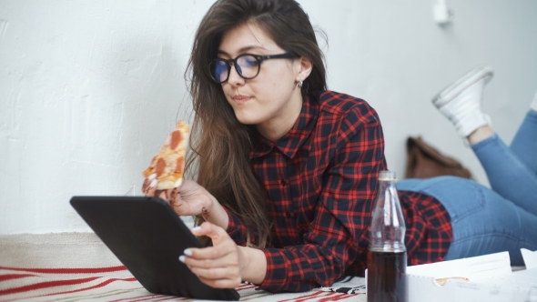 Asian Woman Eating Pizza and Looking at Digital Tablet Computer at Home