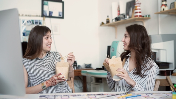 Smiling Young Businesswomen Having Lunch At Table In Office