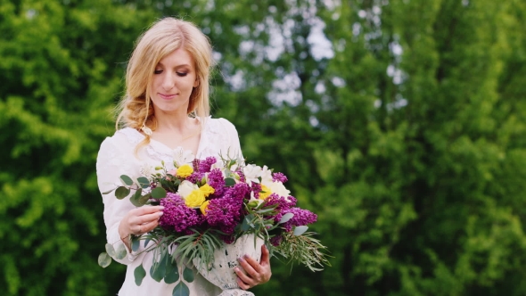 Beautiful Blonde Woman With a Bouquet of Lilacs. It Stands on a Background of Green Bushes