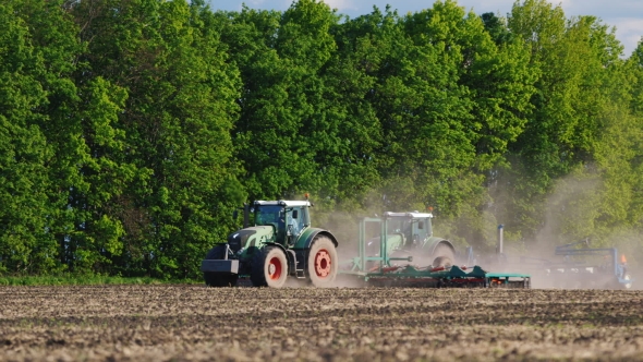 Works In The Field - Two Tractors Seeded Field On a Background Of Green Trees