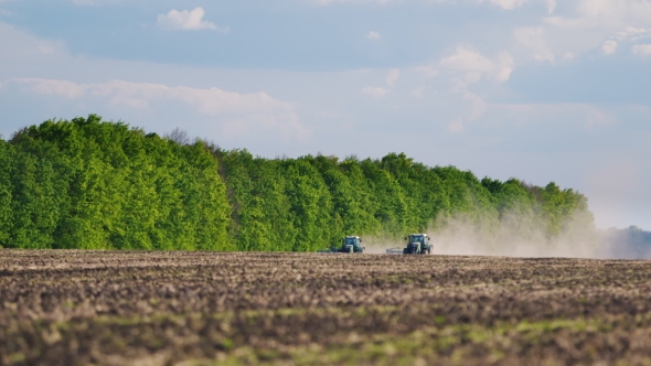 Tractor In a Field Is Planting. In The Background Forest And Blue Sky