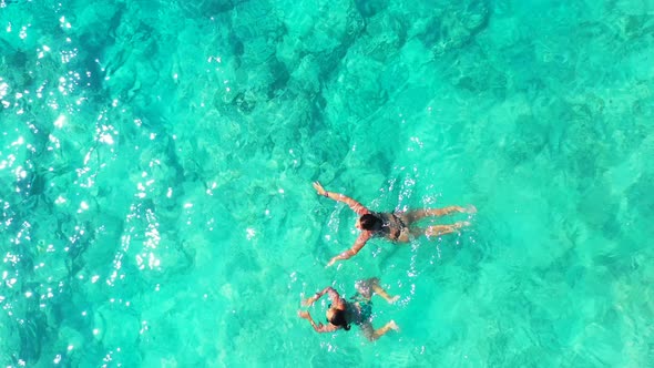 Girls swim on crystal emerald water of shallow lagoon with beautiful rocky seabed texture reflecting