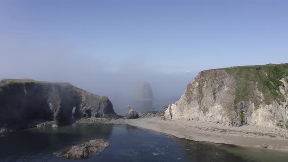 Aerial retreat from eroded sea arches in rugged grassy coastal islet