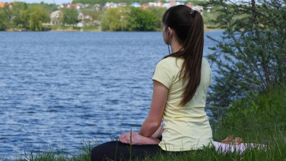 Girl Sitting On The Grass And Relaxing Meditating On The Beach Beside The River