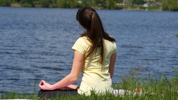 Girl Sitting On The Grass And Meditate Beside The River