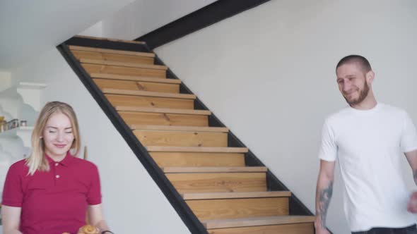 Happy Young Tattooed Man Walking Down the Stairs and Kissing Blond Wife and Daughter in the Morning