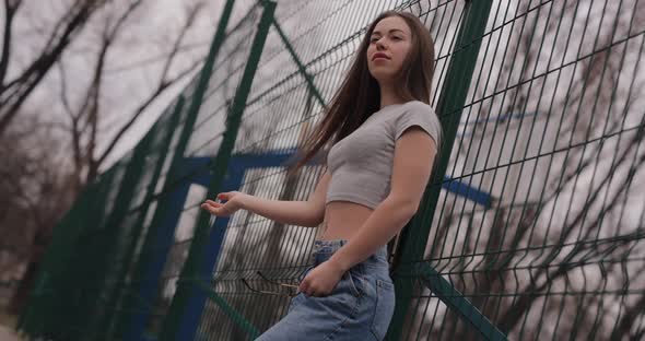 Cute Girl Standing Near Fence on a Stadium in a Park Wearing Eyeglasses